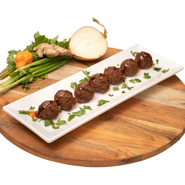 Seven Caribbean meatballs with sauce and parsley on a white plate, with fresh ingredients.