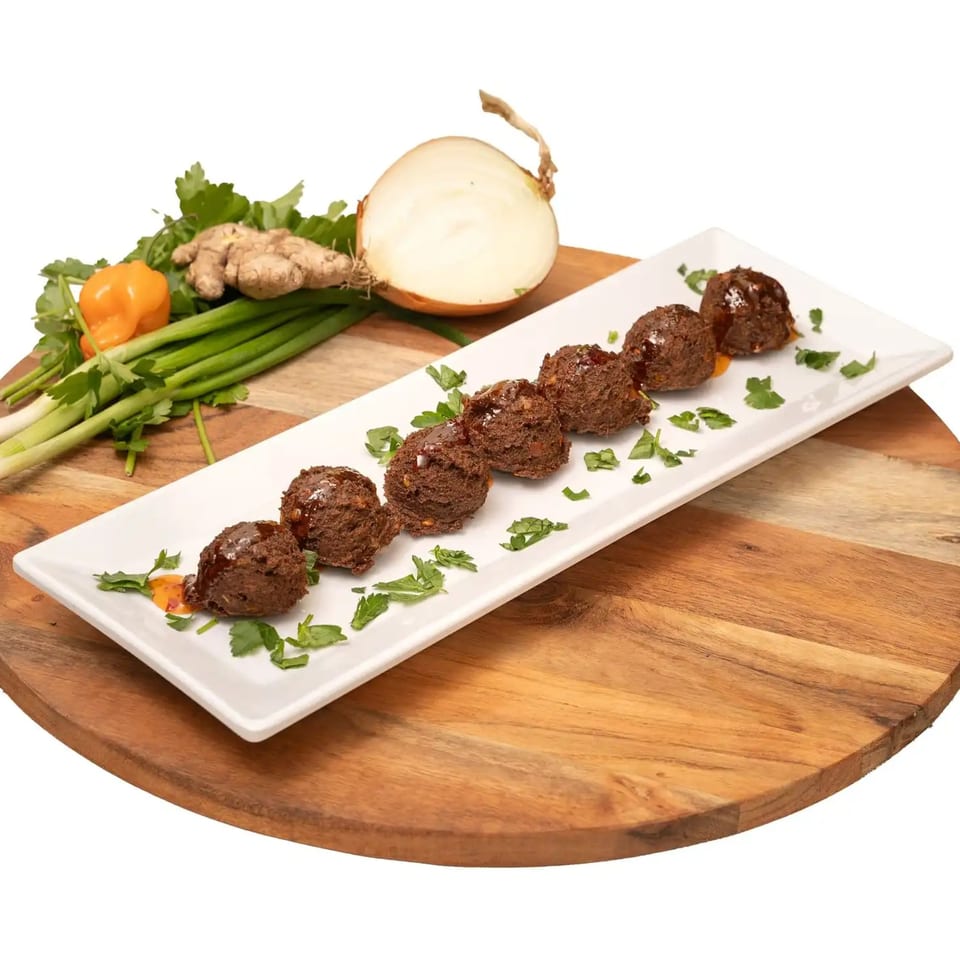 Seven Caribbean meatballs with sauce and parsley on a white plate, with fresh ingredients.