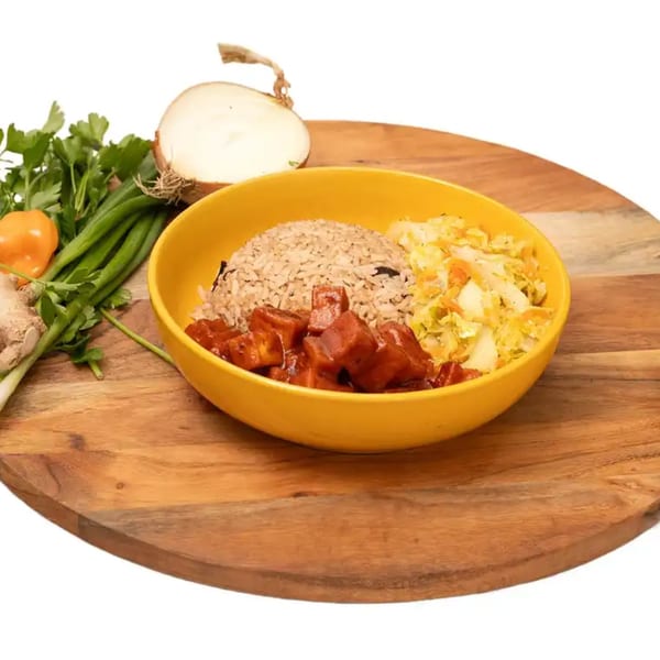 A vibrant Caribbean meal with rice, red stew, and cabbage in a yellow bowl, surrounded by fresh ingredients.