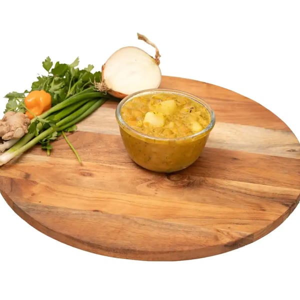 A bowl of Caribbean stew with potatoes, alongside fresh ginger, habanero, scallions, parsley, and onion.