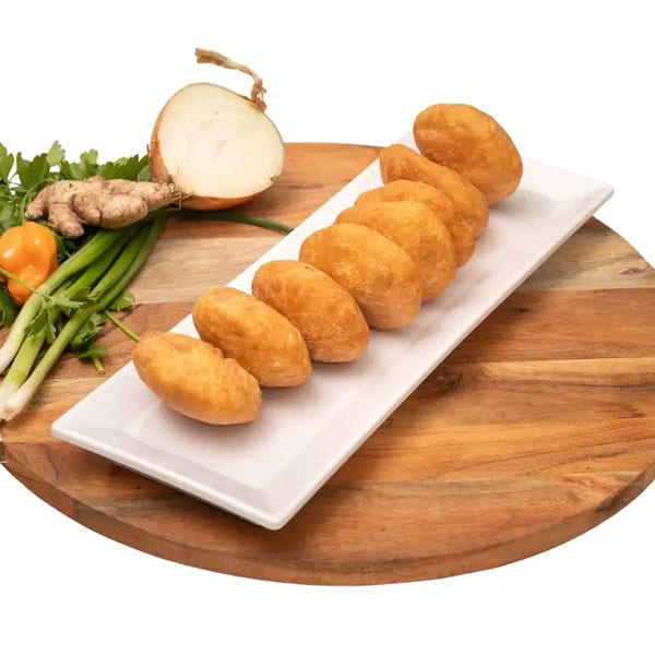 Golden brown Caribbean fried dumplings on a white plate, with fresh ginger, onion, and herbs.