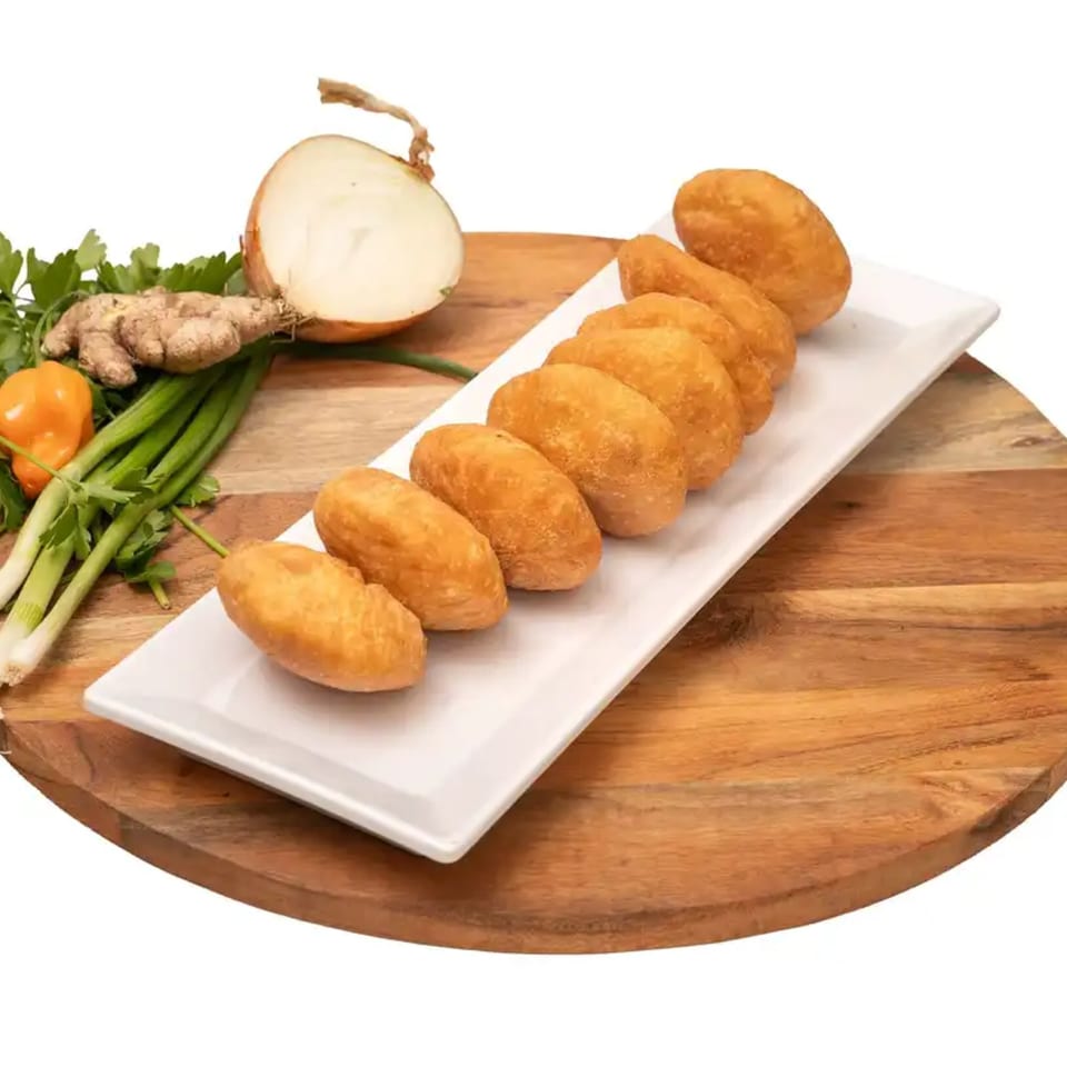 Golden brown Caribbean fried dumplings on a white plate, with fresh ginger, onion, and herbs.