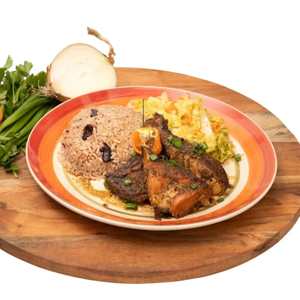 Caribbean jerk chicken with rice and peas, cabbage, and a scotch bonnet pepper on a colorful plate.