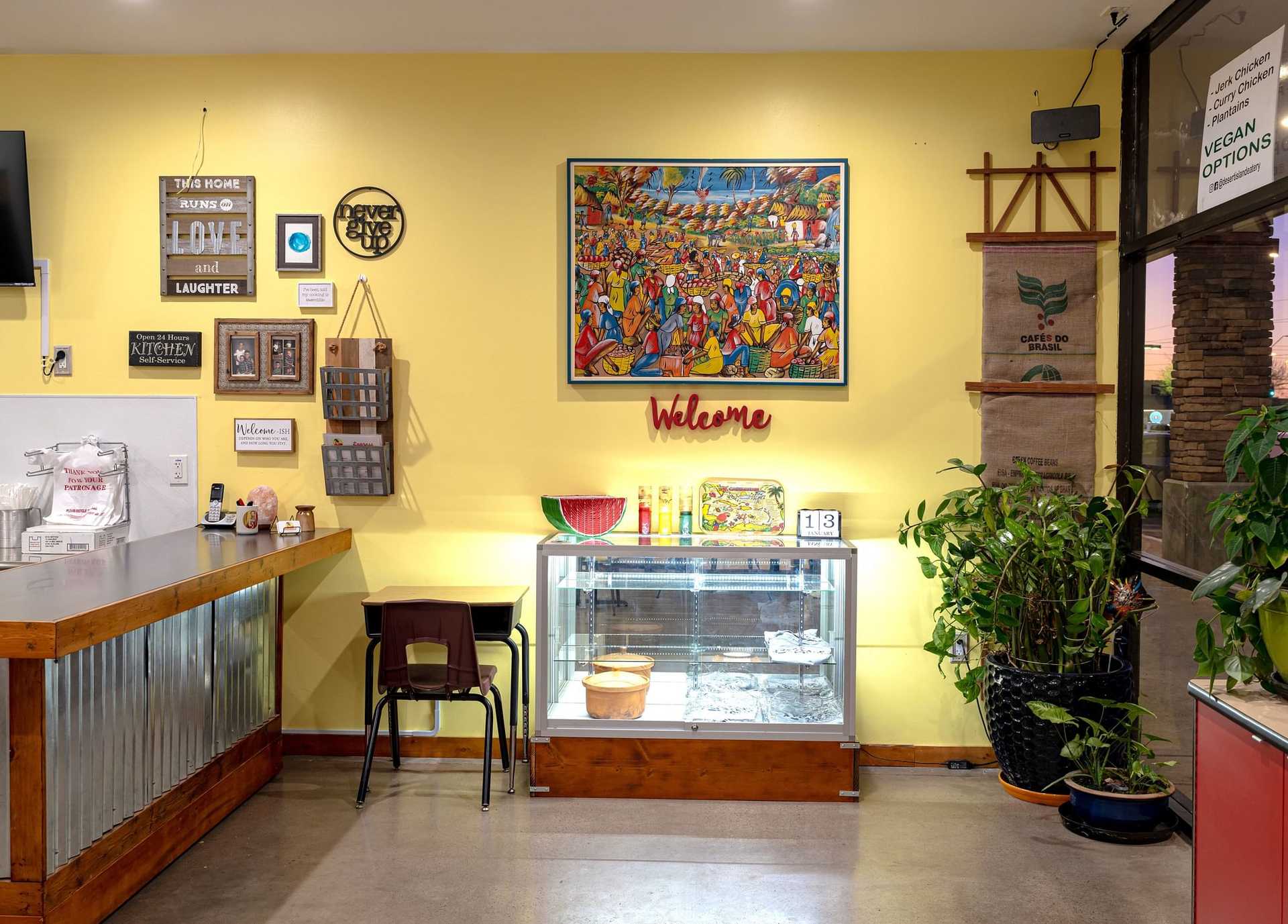 Colorful restaurant corner with decor and welcome sign, highlighting artwork and a small display case.
